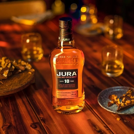 A bottle of Jura whisky and glasses on a table with small plates of sweet treats.