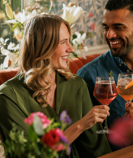 An image focusing on 2 customers enjoying Valentines Day Date Night cocktails and celebrating with a cheers sat at a table within the interior seating area at The Crown.