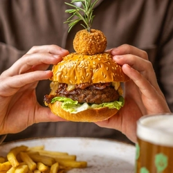 A close up image of a person holding a Signature Burger sat at a table within the interior restaurant seating area at a Chef & Brewer venue.
