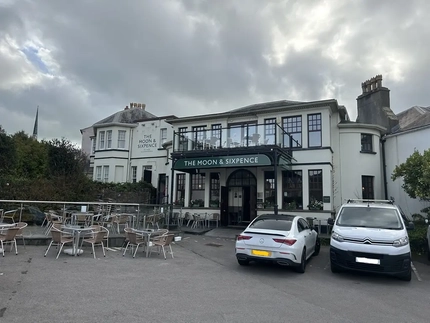 The exterior of the Moon & Sixpence showing outdoor seating, and part of a car park.