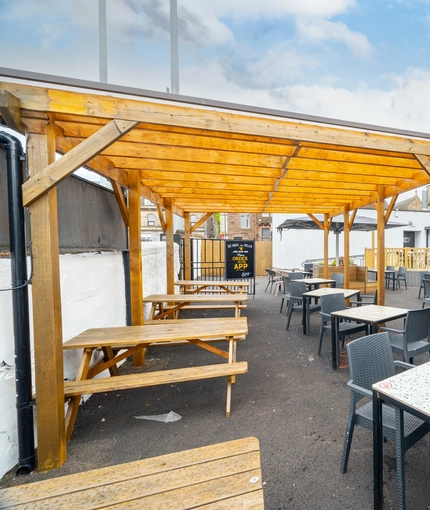 The exterior beer garden seating area at the Counting House in Dumbarton, with wooden picnic tables, padded booth seating, and an under cover area.