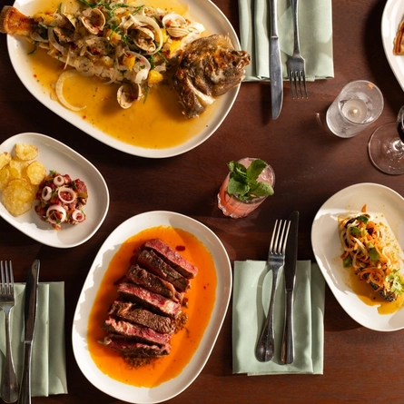 An advertising image of a selection of dishes and various drinks sat on a table within the interior restaurant and seating area at The Ubiquitous Chip.