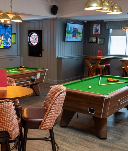 The interior games area at the Devonshire Arms in Sheffield, with two pool tables, a dartboard, TVs on the walls, and restaurant seating.