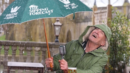 A image of Larry Lamb sat in a beer garden with a umbrella up whilst its raining with a pint of Level Head.