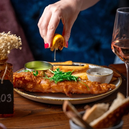 A serving of Atlantic cod and chips with a staff member squeezing a lemon to flavour the Cod served in the internal restaurant at the Sherlock Holmes in Greater London.