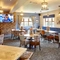 The interior restaurant seating area of The Flying Horse in Heald Green, with wooden tables, upholstered chairs, and a TV on the wall.