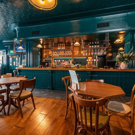 The bar in the Tattersall Tavern, with some tables and chairs near it.