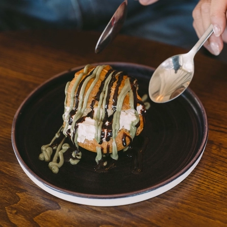 Dessert pastry topped with ice cream and drizzled with chocolate and green sauce, served on a dark plate.