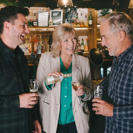 A group of friends stood round the bar with low and no drinks in a Greene King venue.