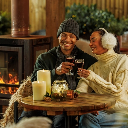 An image of 2 people enjoying festive drinks within the exterior beer garden seating area with fireplace at The Watermill.