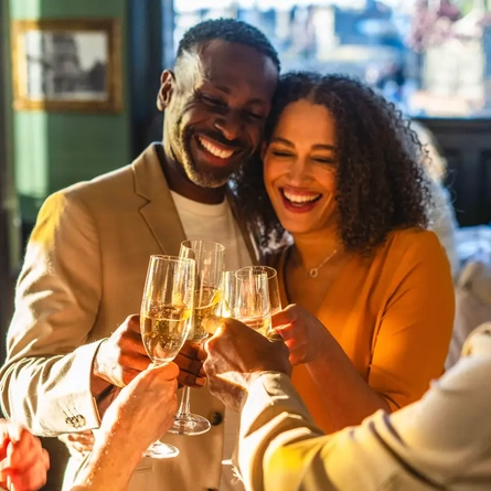 A couple cheersing with a group, with drinks in their hands.