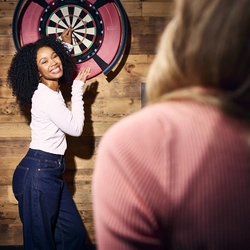 An image showing 2 friends enjoying a game of darts within the interior games area at a Flaming Grill venue.