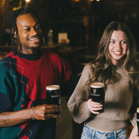 An image of 3 friends stood holding pints of Guinness within the interior of a Greene King venue.