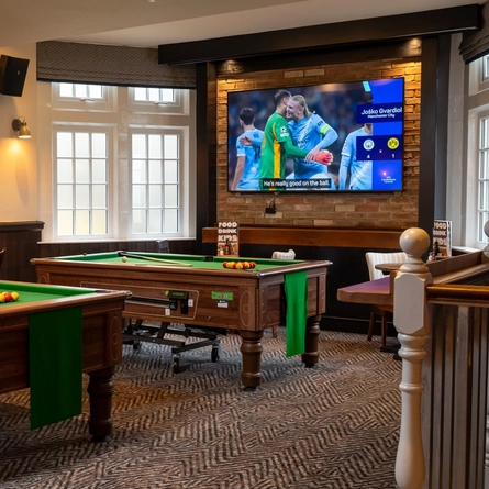 The interior pub gaming area of The Railway, with two pool tables, a TV on the wall, and restaurant tables.