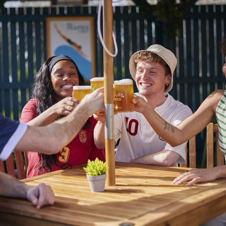 A mixed group of people seated at an outdoor table holding drinks.