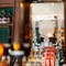 A mirror engraved with the words "Lord Raglan" and filigree patterns, and bottles of whisky and other alcoholic spirits on wooden shelves, behind the bar at the Lord Raglan.