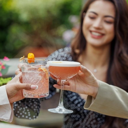 An exterior image of a group of people celebrating with a cheers with various cocktail style drinks available at Crafted venues.
