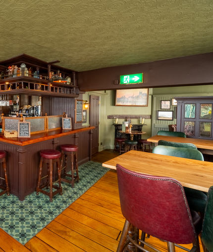 The bar and interior restaurant seating area at The London Apprentice, with bar stool seating, a fireplace, and ornaments on a wooden shelf above the bar.