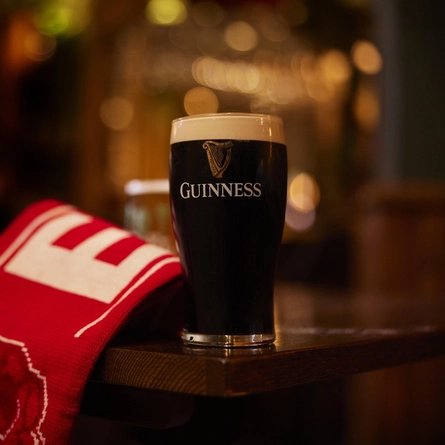 A pint of Guinness on a table next to a sports team scarf.