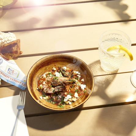 An advertising image showing a seafood dish and 2 drinks sat on a table within the exterior beer garden seating area at a Chef & Brewer venue.