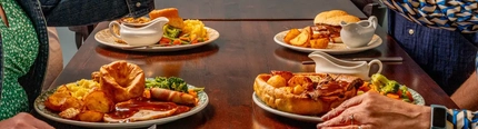 Four people raising their glasses in a toast over their roast dinners.
