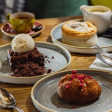 An advertising image showing a selection of desserts from the Prix Fixe menu sat on a table within the interior restaurant seating area at The Four Oaks.