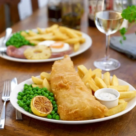 A plate of fish and chips and a plate of gammon and chips
