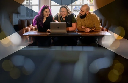 People sitting around a laptop in a seating area of a Greene King pub.