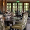 A close up view of a circular wooden table in the interior restaurant seating area of The Hollybush in Lichfield, with upholstered chairs around the table, and wooden beams and floor to ceiling windows visible in the background  