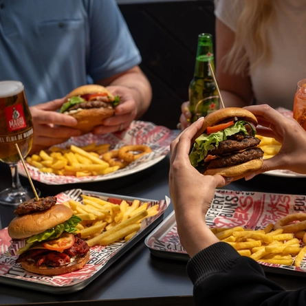 A pair of hands holding a burger in front of a table of food.