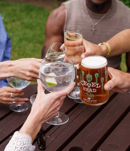 A close up image focusing on various drinks being held within an exterior beer garden seating area.