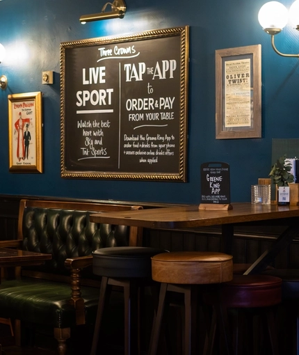 The interior restaurant seating area with TV screen and various chalkboard advertising signage at The Three Crowns.