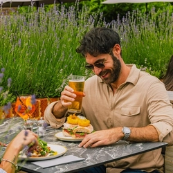 An image of two people enjoying two dishes from the lunch menu and drinks within the exterior beer garden seating area at a Crafted venue.