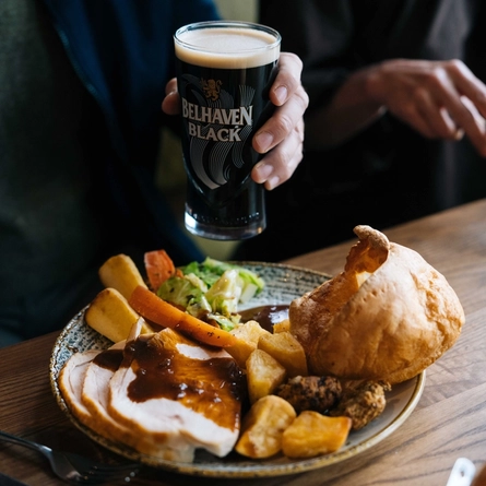 A close up image of a person sat at a table within the interior restaurant seating area enjoying a pint of Belhaven Black and a roast at a Heritage venue.