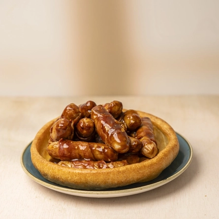Pigs In Blankets with BBQ sauce, served in a giant Yorkshire Pudding on a plate.