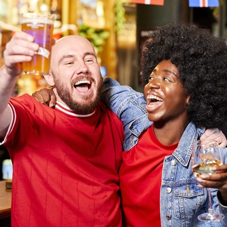 Two people holding a drink and cheering.