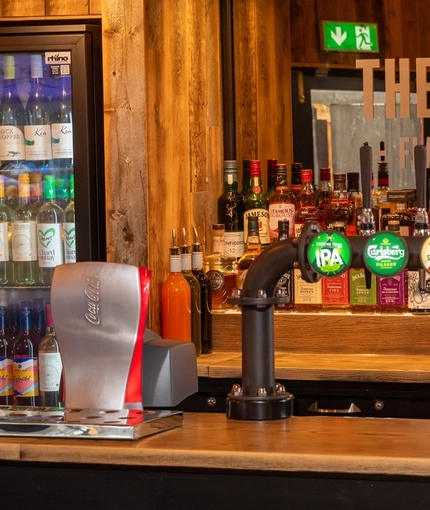 A close up view of the bar inside The Amington in Tamworth, with bottles of alcoholic spirits on a wooden shelf behind the counter, and a TV on the wall.