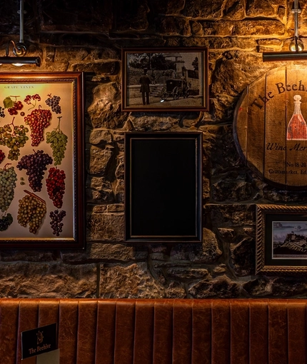 An interior restaurant seating area at The Beehive Inn, with a long upholstered booth seat, and a stone wall decorated with framed artwork, and a TV on the wall.