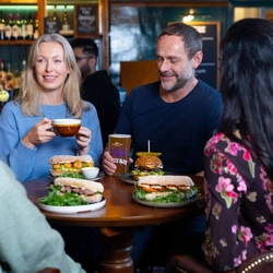A group of friends sat in the interior restaurant and seating area in a Urban Social venue, enjoying meals off the lunch menu and drinks.