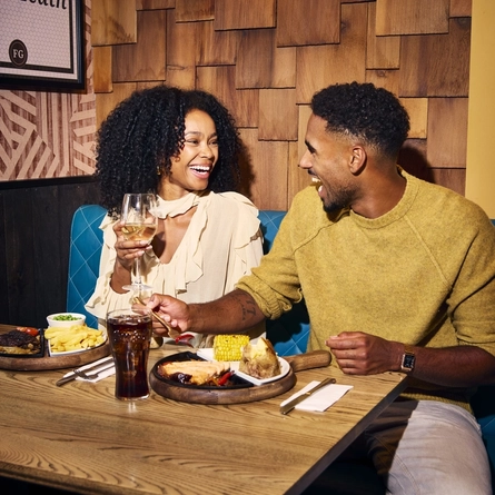 An image showing 2 friends sat at a table enjoying food and drinks within the interior restaurant seating area at a Flaming Grill venue.