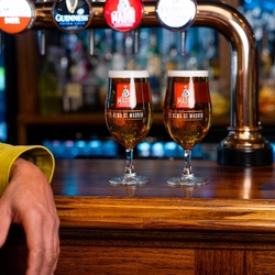 Two pints of Madri on a bar next to a man's arm.