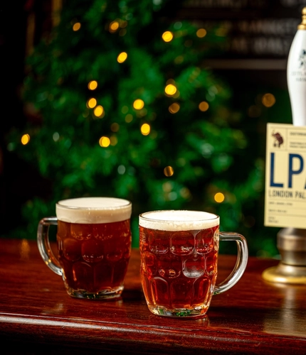 Two tankard pint glasses of beer on a bar.