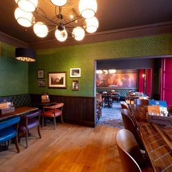 An interior restaurant seating area at The Beehive Inn, with an upholstered booth seat, and framed artwork on the green wallpapered walls.