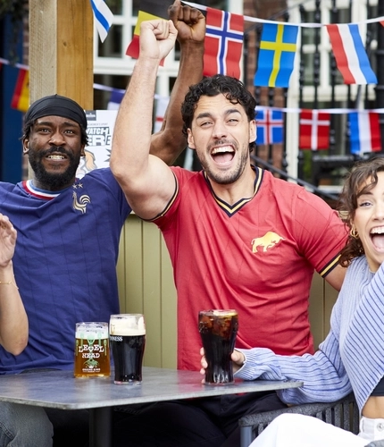 A mixed group of people sitting at an outdoor table, enjoying watching sport and drinks.