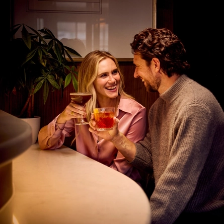 An image featuring 2 people sat at a table within the interior seating area of the venue with a selection of drinks at The White Horses.