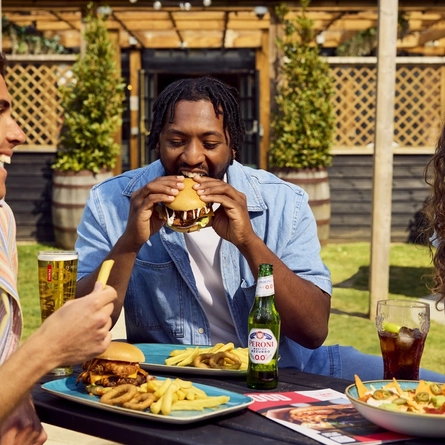 A group of friends all sat round a table with meals and drinks served in the exterior beer garden at a Flaming Grill venue.