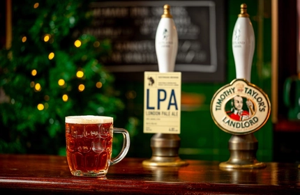 A tankard pint glass of beer on a bar.