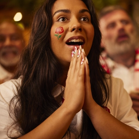 An image of a woman wearing a sport team shirt, watching a sporting event.
