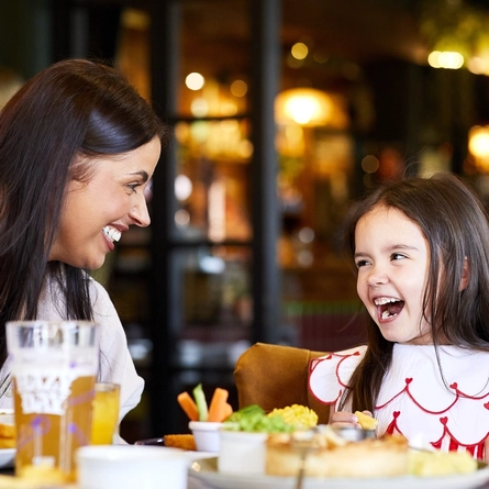 A child seated at a table with their parent, enjoying food.