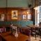An interior restaurant seating area at The Plough, with upholstered chairs and booth seats, and framed artwork on the wood panelled wall.
